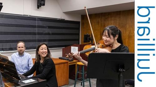 woman playing violin alongside two people seated at a piano